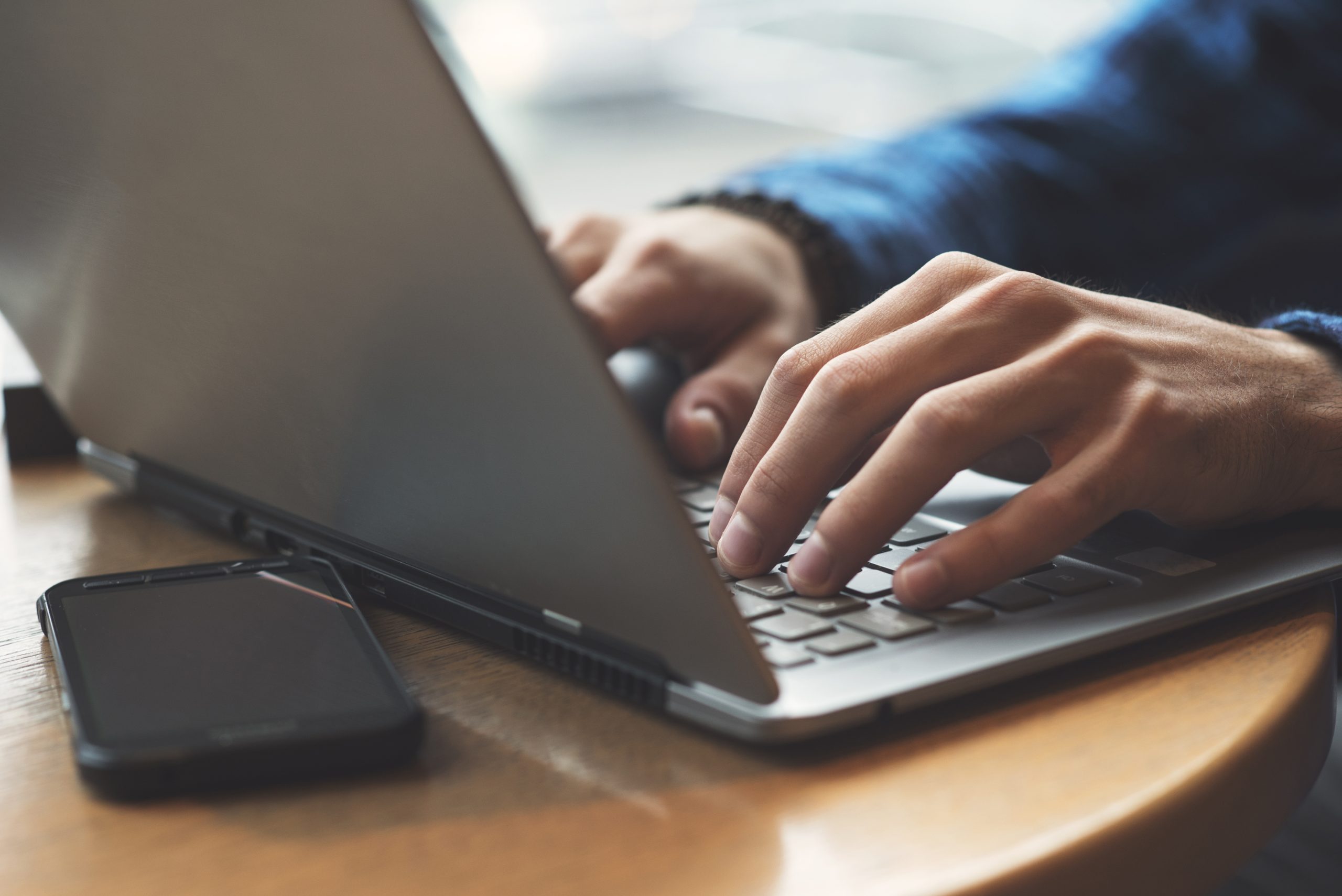 Hands typing on a laptop keyboard next to a smartphone